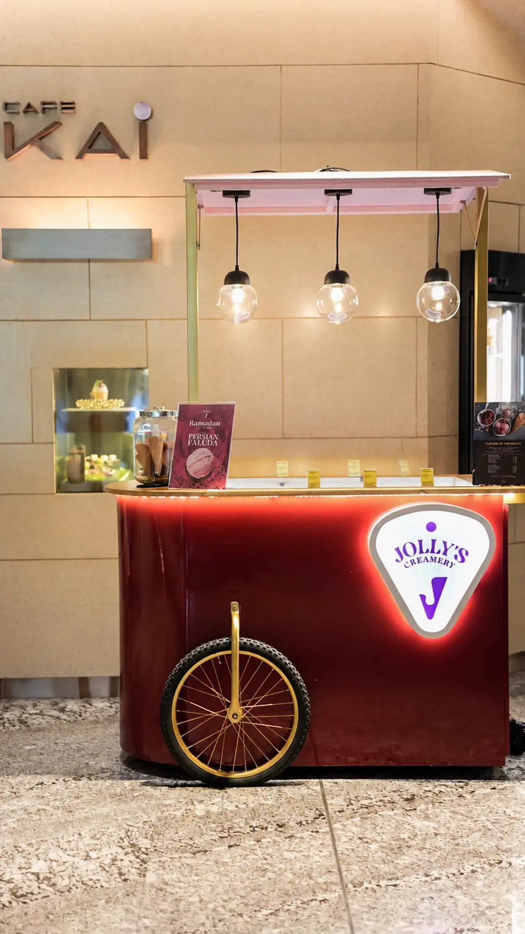 A red Jolly's cart with pendant lights beside Café Kai in a hotel lobby
