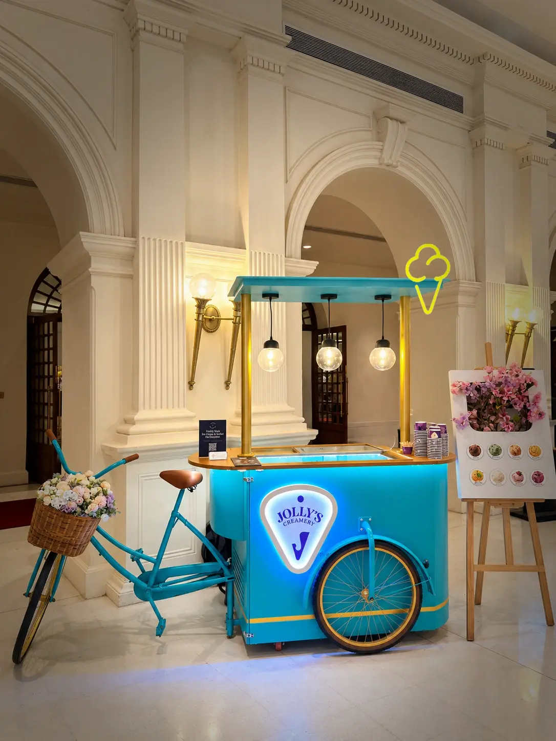 Bubblegum Blue Jolly's cart with a blue bicycle and flower basket under the arches of a hotel lobby
